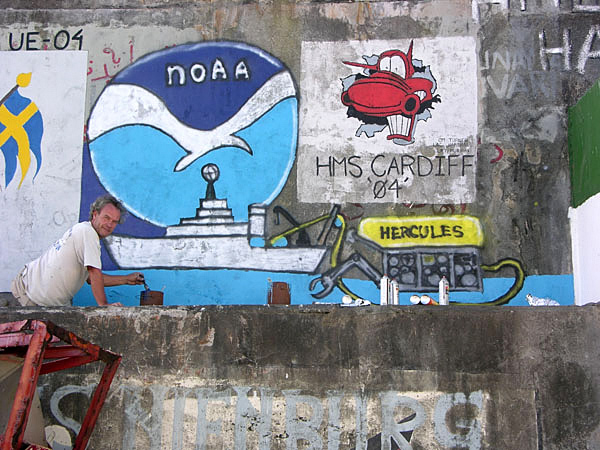 NOAA Ship Ronald H. Brown Chief Boatswain Bruce Cowden putting the finishing touches on a painting at the port in Ponta Delgada. It is a tradition in some ports for visiting ships to paint a logo, emblem or some other image to commemorate their visit.
