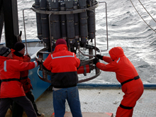 Mike Kong, Vladimir Bakhmutov, Dan Torres, and Russ Hopcroft help guide the swinging rosette to its pallet during a swell. The rosette weighs 760 pounds even without bottles or instruments and is deployed and recovered by a winch-wire. During heavy seas or a swell, the rosette can be hard to control both on deck and in the water.