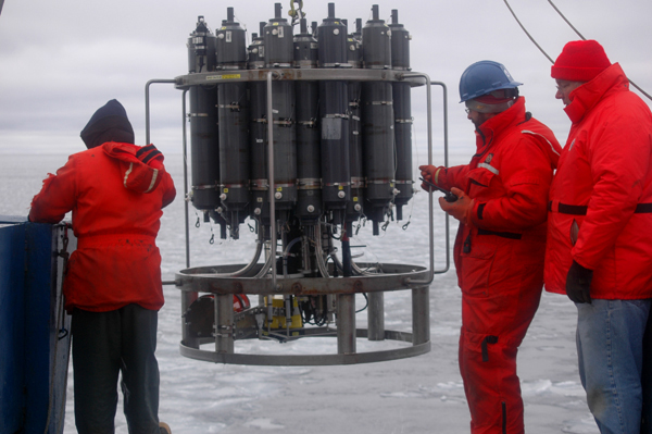 Mike Kong, Dan Torres and Marshall Swartz stand by as the conductivity, depth and temperature (CTD) recorder, mounted to the circular rosette along with many Niskin water bottles, returns after a cast at one of the iciest stations. The CTD and associated recorders help define properties of the water samples, which helps scientists understand where the sampled water came from, and where it is headed.