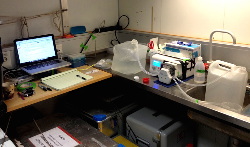 What microbiology may look like in a little corner of a small storage room on a large ship. Seawater obtained from Niskin bottles were collected in 10-liter carboys, transferred to this workstation, and pumped through filters using a peristaltic pump. The filters containing microbial cells were immediately frozen and awaited transportation to Alaska for genetic sequencing.