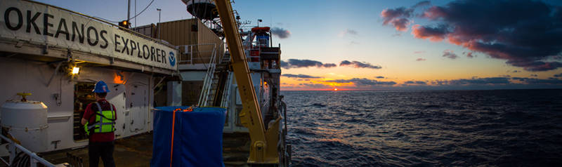 The sun is seen setting off the starboard aft of NOAA Ship Okeanos Explorer.