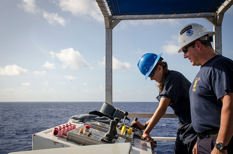 Commanding Officer, CDR Eric Johnson, oversees ENS Brianna Pacheco as she navigates the ship from the aft conning station. ENS Pacheco demonstrated her navigation skills to bring a buoy thrown off the the ship around to the starboard side for retrieval. An official letter was attached to the buoy – designating her as a qualified Officer of the Deck (OOD) underway on NOAA Ship Okeanos Explorer! This means she possesses all the skills required to maintain a competent navigation watch, and she is thoroughly familiar with the ship, its operating and safety systems, and can effectively take care of her own safety as well as that of the ship.
