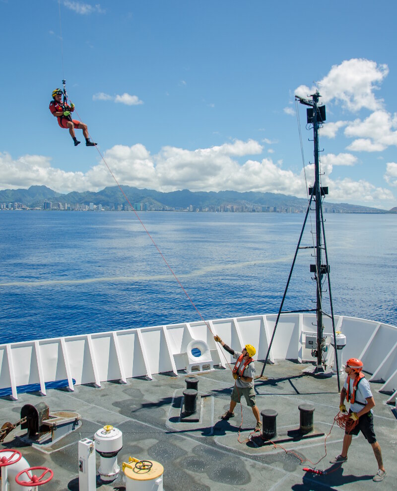 A U.S. Coast Guard rescue swimmer is deployed to the bow of NOAA Ship Okeanos Explorer during a training drill off the coast of Oahu, Hawaii.