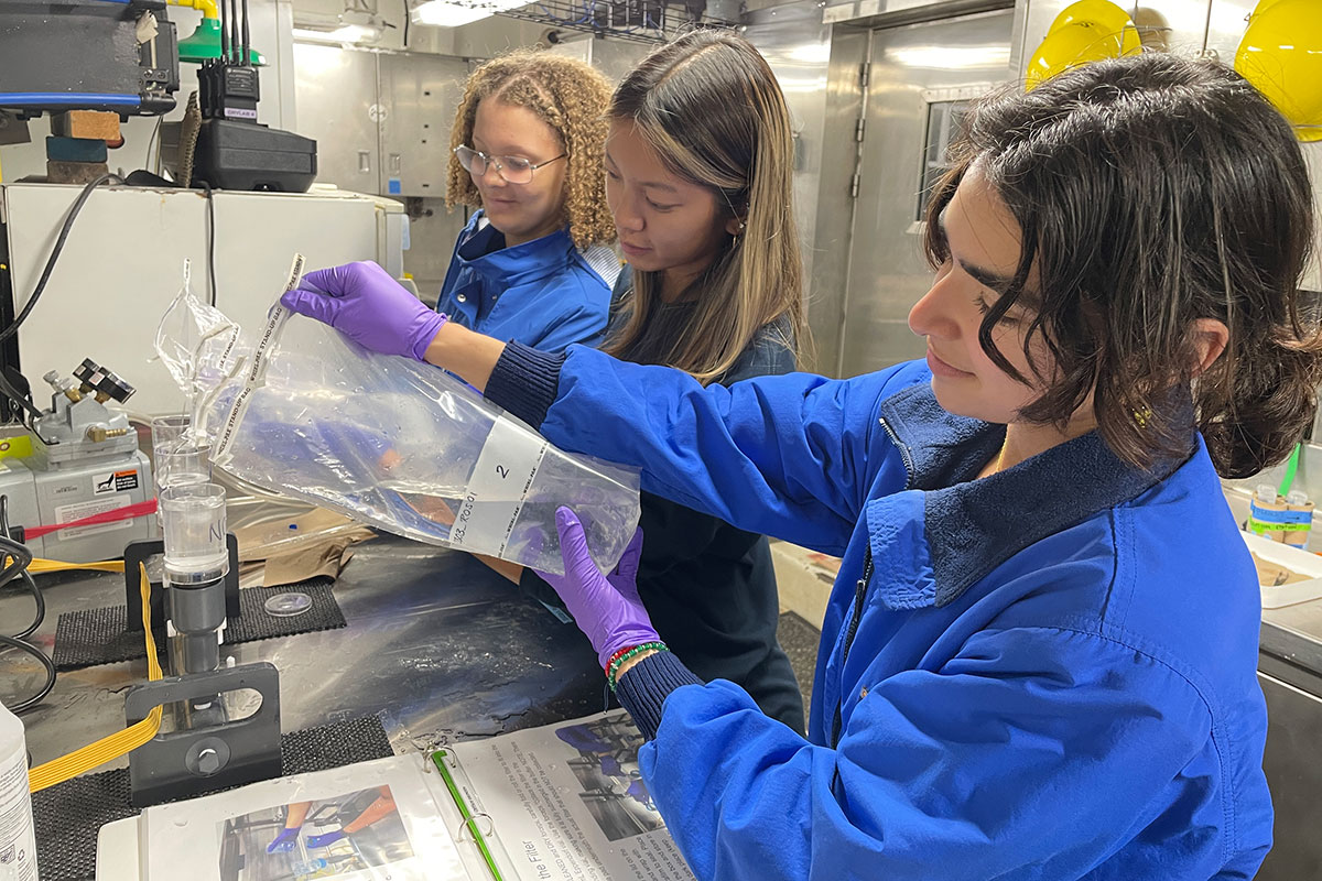 Three explorers-in-training filter water samples for environmental DNA collection in the wet lab on NOAA Ship Okeanos Explorer.