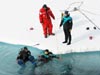 Ice Divers enter the water while a Coast Guard Petty Officer tends the line and a safety diver stands by.