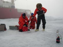 Scientist lower containers through a hole in the ice to collect water samples from different depths.