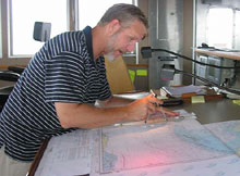 First Mate Mike Schoeller checks his charts to confirm the ship's faster-than-expected transit time to its first dive location.