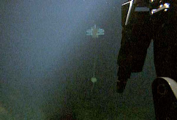 The suspended current meter is seen hanging below its float pack out in the distance beyond the manipulator arm of the ROV. 