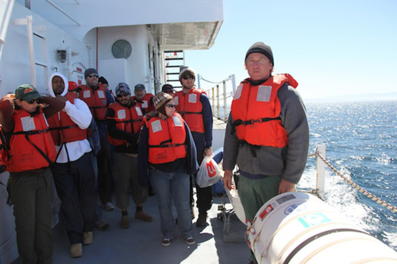Scientists don life jackets during an abandon ship drill on the upper deck. Ian Lawrence (right), the ship’s first mate, shows the group how to release the life boat in the event of an emergency.
