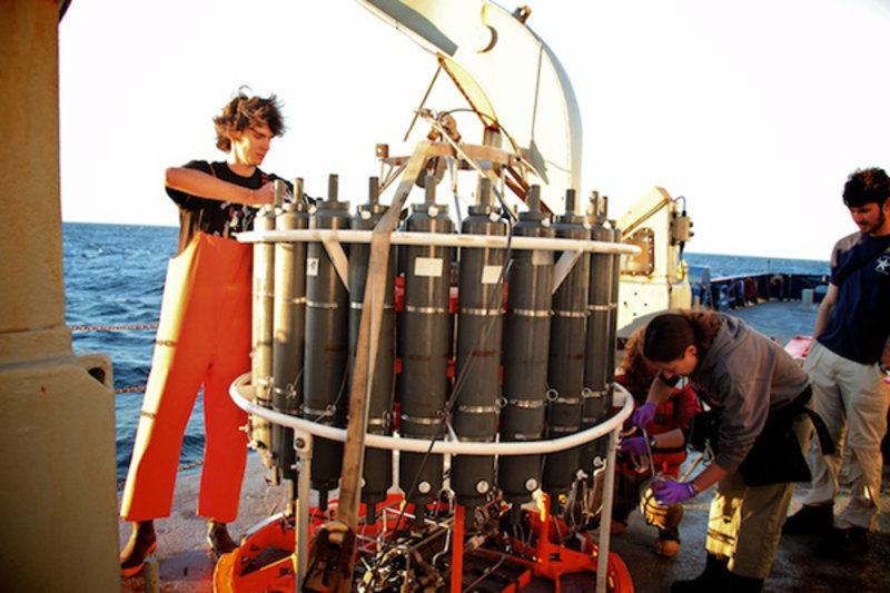 Figure 1. Ben Grupe (left) prepares the conductivity, temperature, depth (CTD) bottles for deployment. This is one instance when being tall comes in handy. Normally, scientists have to climb onto the white frame to cock the bottle caps. As the CTD is lowered into the ocean, a computer monitors the data and orders bottles to snap shut, collecting water samples from different depths.
