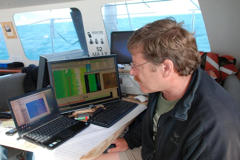 Dr. Chris Goldfinger, project PI, watches the multibeam screen as data returns in near-real time. Bathymetric and backscatter data obtained from multibeam sonar are used to determine seafloor depth as well as indicators of the type of sediment (hard or soft bottom) that is below.