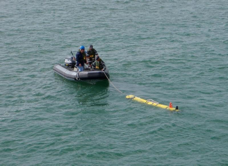 Explorers often use a small boat to attach a line or cable to the AUV. In this sea-test, they used a ridge-hulled inflatable boat (RHIB), which is a hard-bottomed boat with inflated rubber sides. Once the AUV is secure, they tow it over to the support ship to hook the AUV to the crane and lift out of the water.