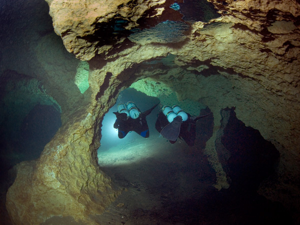 Two divers using traditional back mounted open circuit scuba equipment to explore a cave.