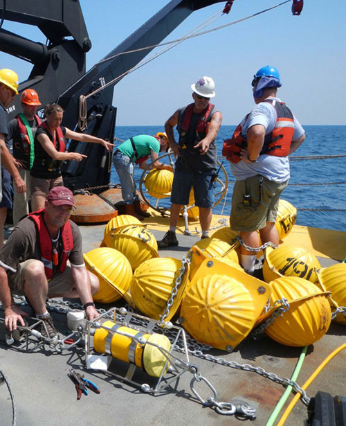 Dr. Brendan Roark (Texas A and M) attaching instruments to the mooring while scientists and deck crew discuss deployment logistics.