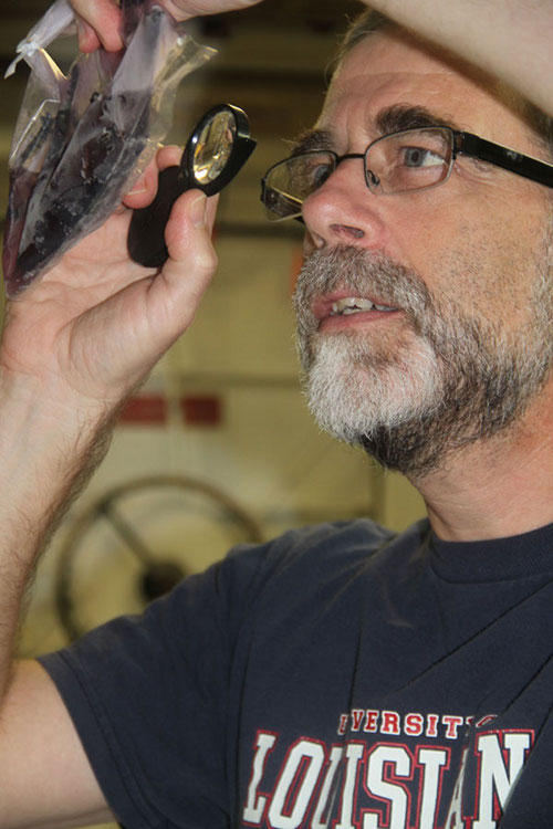 Dr. Scott France examines a sample of coral collected on the first leg of this mission. This deepwater sea fan in the family Plexauridae, appears yellow when alive but after being preserved in ethanol for DNA studies has leached purple pigments.