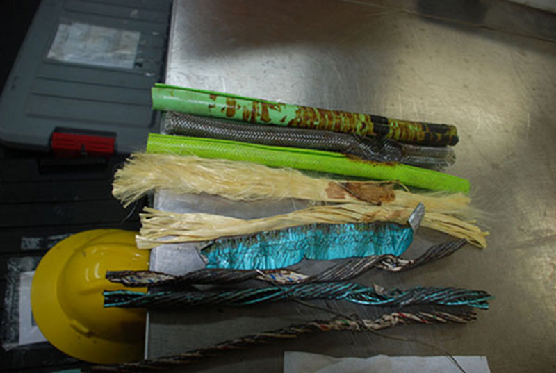 Shown here are the individual components of the damaged ROV cable (a bit out of order). At the top is the vinyl outer shell, the yellowish Kevlar fibers, a metal casing, green inner vinyl shell, metal shielding, and electrical conduit. Across the bottom right of the picture is a thin metal wire that is actually a casing containing four strands of fiber optics.