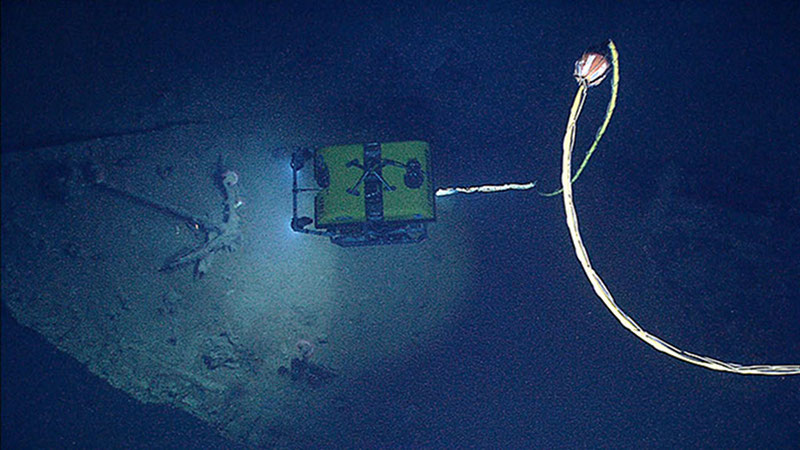 NOAA's Seirios Camera Platform, operating above the Little Hercules ROV, images the ROV and an anchor inside the bow of the shipwreck. Copper sheathing outlines the shape of the bow as the wood has nearly all disintegrated after more than a century on the seafloor. Image courtesy NOAA Okeanos Explorer Program.