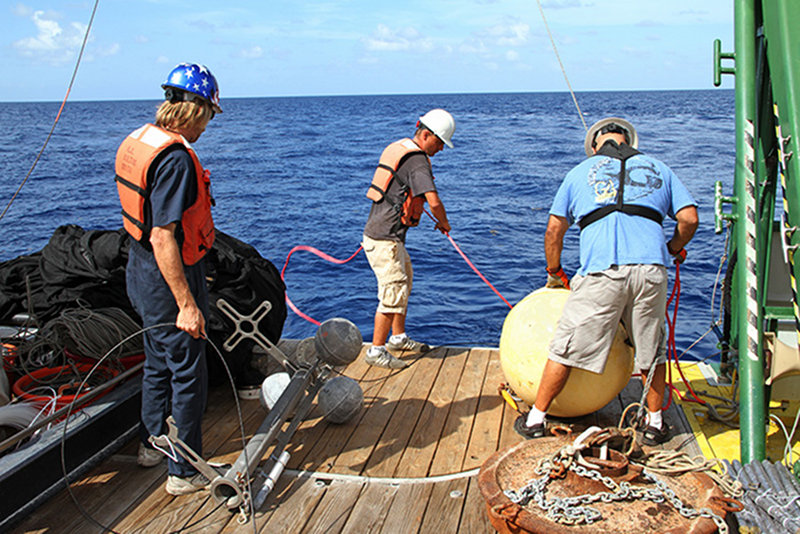 Cedric Guigand, University of Miami (center) and crewmembers of the Walton Smith deploy a light trap mooring over the stern of the vessel.