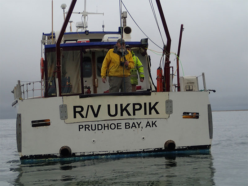 Encountering polar bears along the beach of the survey area was an ever­present danger whenever people were sent ashore. Here, scientists and crew aboard R/V Ukpik keep a close watch over the shore party deploying the magnetometer base station until the party returns.