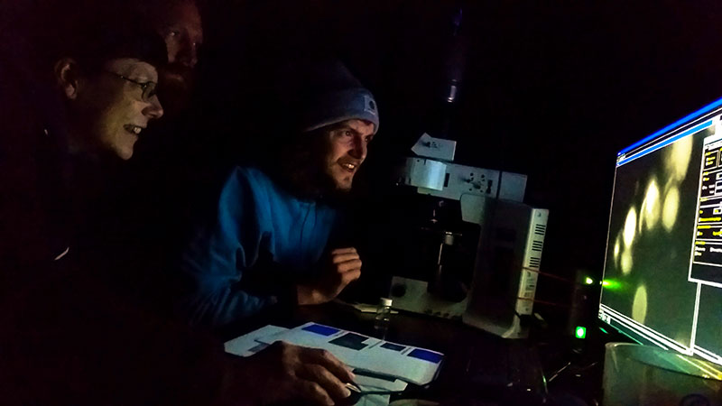 Kyle Dilliplaine and Eric Collins demonstrate their research on fluorescence and microbes to Sandra Thornton.