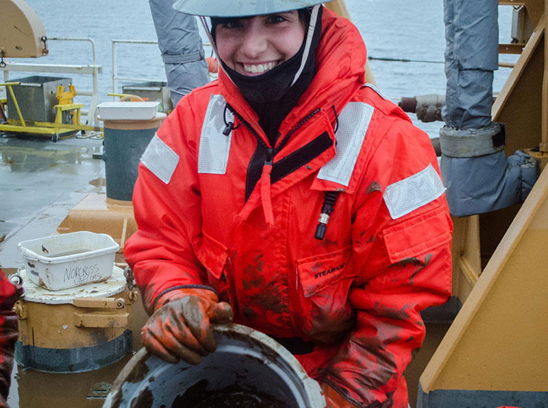 Lauren Sutton displays a bucket of mud from the trawl that contains various organisms, including sea stars and mollusks.