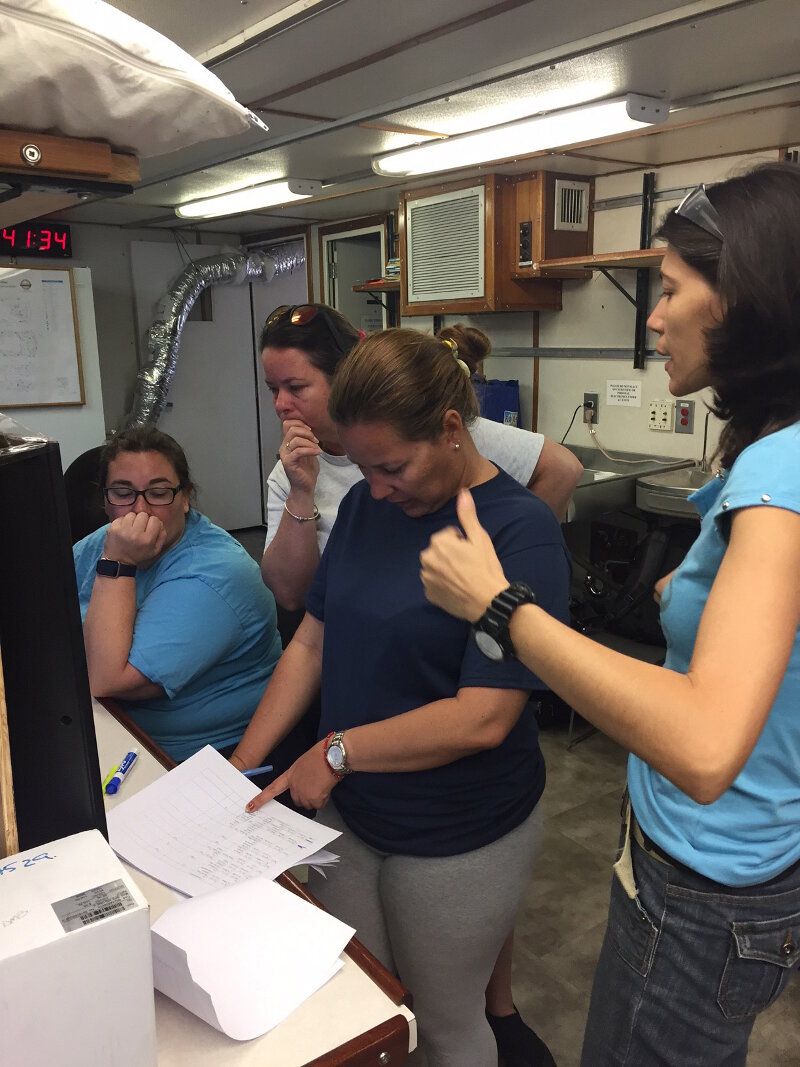 Part of the team gathers around a work station to review cruise information (left to right: Stephanie Farrington, Patricia González Sánchez, Cris Diaz, and Linnet Busutil López).