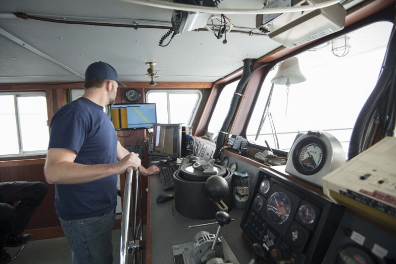 R/V Laurentian captain Beau Braymer pilots the vessel from the wheelhouse. A screen on the cabin’s portside wall relays the sonar feed and survey navigation information to help the captain maintain the correct course to ensure the sonar travels along parallel, overlapping lines.