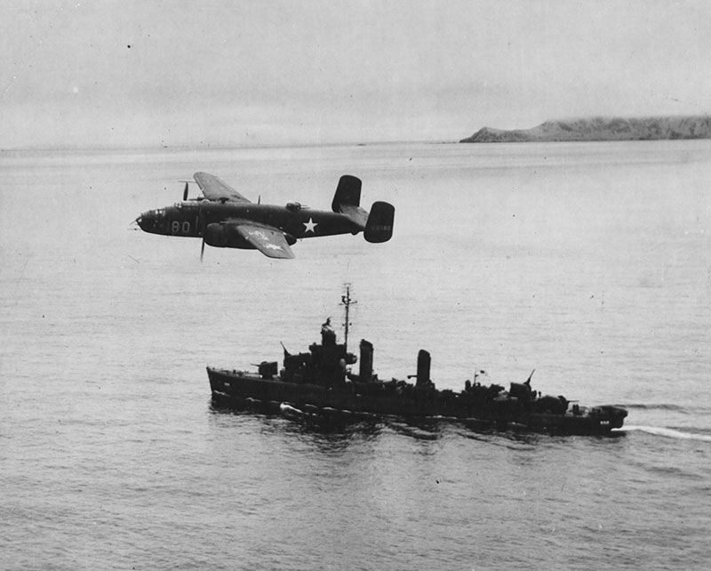 A North American B-25 Mitchell Glides over an American destroyer after taking off from Unmak Island for a raid on the Japanese base at Kiska.