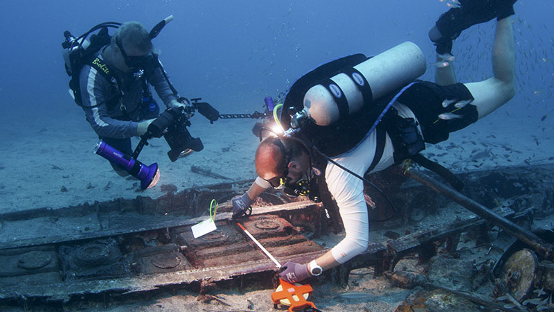 Archaeologists use measuring tapes and underwater cameras to record and document a WWII aircraft site in Papua New Guinea.