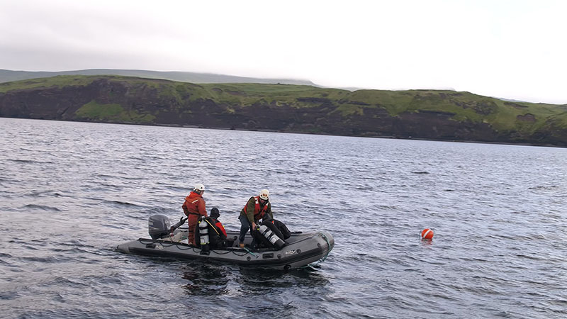 Expedition leads Eric Terrill and Andrew Pietruszka getting ready to dive from a small skiff in Kiska Harbor. The orange buoy marks the dive site.