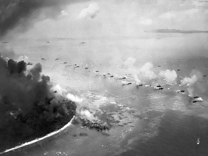 The first wave of LVT(A)s move toward the invasion beaches, passing through the inshore bombardment line of LCI gunboats, 15 September 1944. Cruisers and battleships are bombarding from the distance. The landing area is hidden by dust and smoke. Photographed from a USS Honolulu (CL-48) plane.