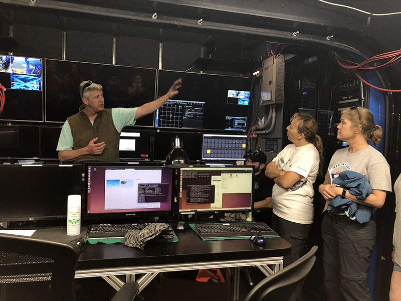 Jason Expedition Leader Tito Collasius gives the science team an orientation to the ROV control room. During dives, three members of the science team will staff the control room in four-hour shifts as watch lead, data logger, and video logger. The Jason team also operates the vehicle with a staff of three: a navigator, a pilot, and an engineer.