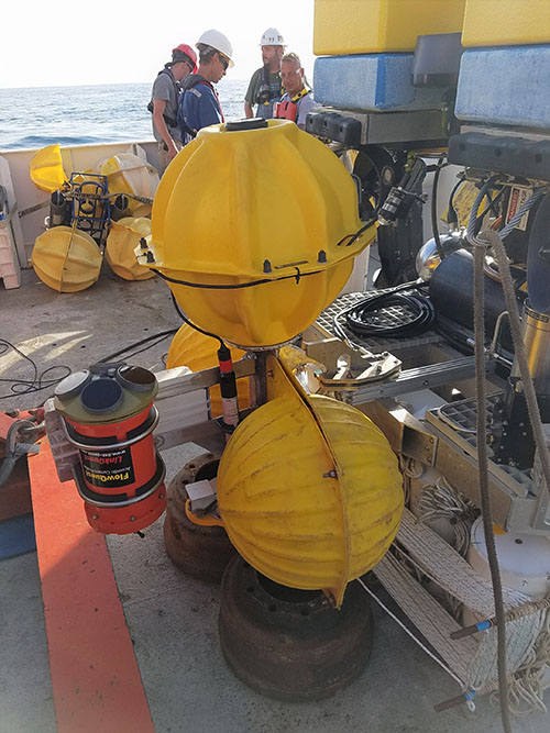 Lander mounted on Odysseus ROV, showing the tangerine-colored ADCP at left and microbial recruitment experiments with rigging secured under the rear platform of the ROV.