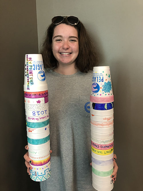OSTC student holding styrofoam cups that were decorated by peers as a classroom activity; these cups will be crushed under the pressure of the ocean, creating a fun souvenir for campers.