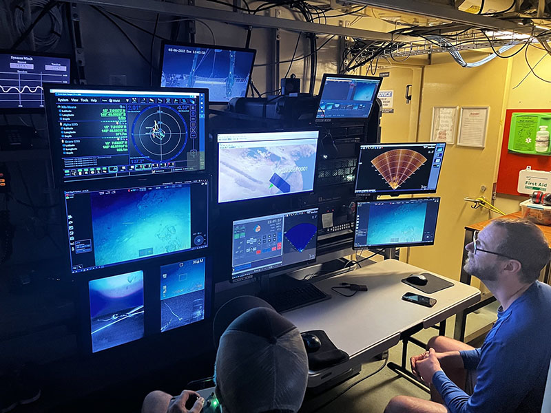 On board Research Vessel Kilo Moana Dr. Andrew Pietruszka, one of the Principal Investigators of the Deepwater Surveys of World War II U.S. Cultural Assets in the Saipan Channel expedition from Scripps Institution of Oceanography, helps guide piloting of a remotely operated vehicle (ROV) that is exploring underwater sites that may contain aircraft wreckage. Dr. Pietruszka is the lead archaeologist of the program. Screens show a live feed from the cameras as well as information on depth and pitch of the ROV. Additionally, a forward-looking sonar is used to guide researchers to objects that are out of the field of view of the cameras. Image courtesy of Kyle Palmer, MARE.