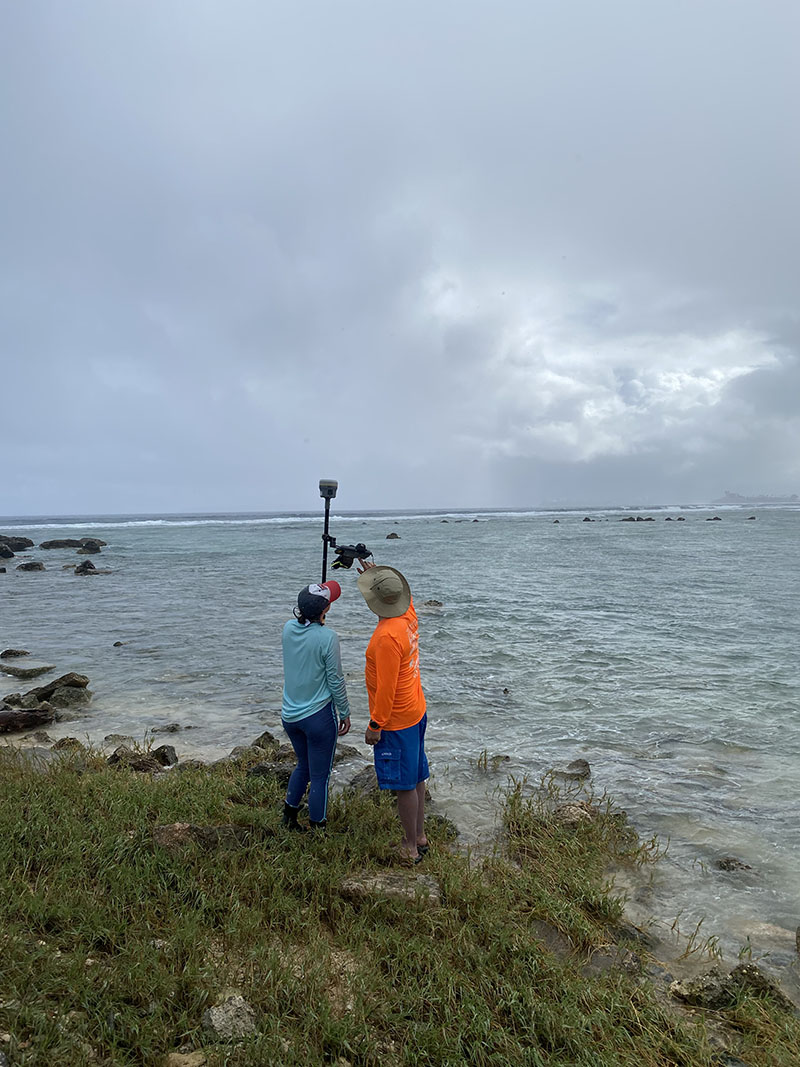 Tahzay Jones instructing Olivia Helinski on how to collect data using Global Navigation Satellite System equipment to capture the vegetation line along the coast at the Asan unit of War in the Pacific National Historical Park.