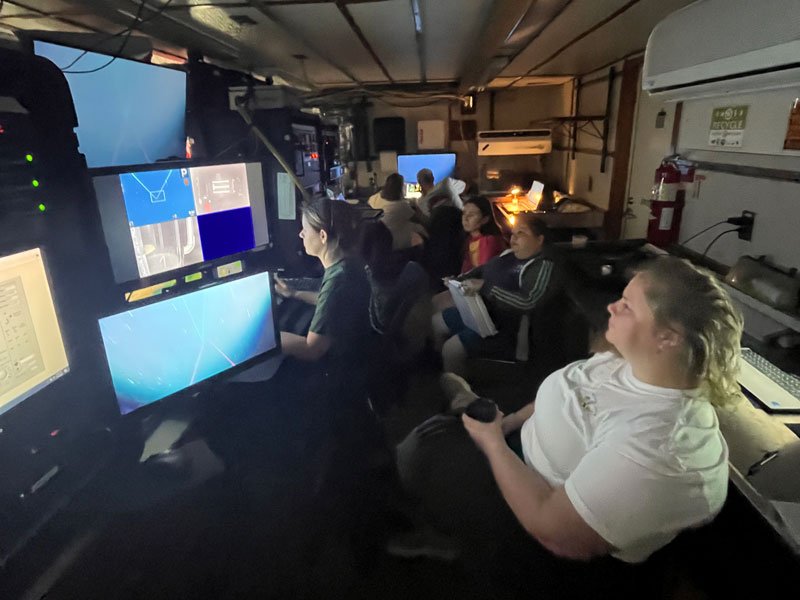 All eyes are on the monitors during a dive. Kirstie Francis, Esther Guzmán, and Courtney Brooks (right side, front to back) watch intently as Samantha Flounder drives the remotely operated vehicle during Exploration of Deepwater Habitats off Puerto Rico and the U.S. Virgin Islands for Biotechnology Potential. In the background, John Reed and Cristina Diaz discuss the possible identity of the organism.