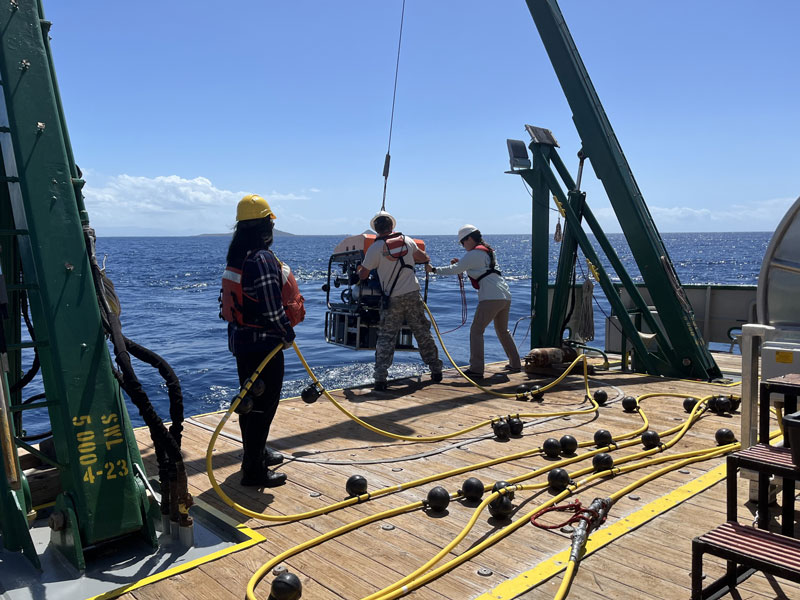 Carol Kim (left) makes sure that the umbilical tether between the ship and the remotely operated vehicle (ROV) is not tangled while Jason White (middle) and Madison Lytle (right) launch the ROV.