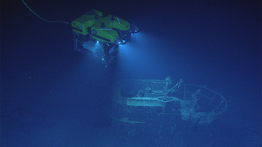 ROV exploring a sunken ship in deep blue water.