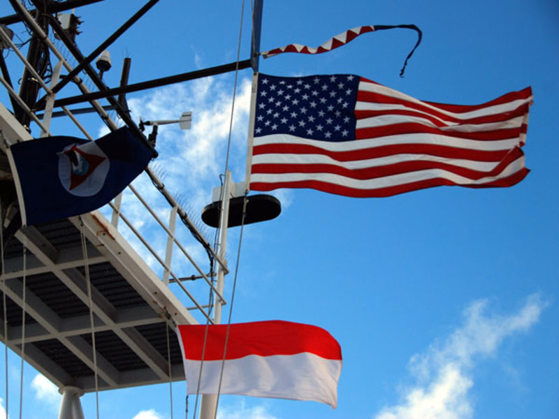 Flags of the United States of America, Republic of Indonesia, NOAA Corps, and Okeanos Explorer Commissioning fly above the bridge.