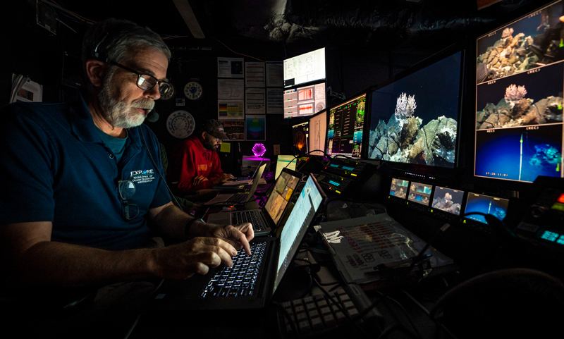 Scott France, biology lead for the second Voyage to the Ridge 2022 expedition and Arvind Shantharam, sample data manager for the expedition, work in the control room of NOAA Ship Okeanos Explorer.