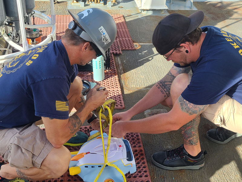 Chief Bosun Jerrod Hozendorf (left) and Boatswain Group Leader James Scott (right) ready the Octoray for launch, checking that the straps are secure and safe for deployment off the back deck of NOAA Ship Okeanos Explorer during the third Voyage to the Ridge 2022 expedition.
