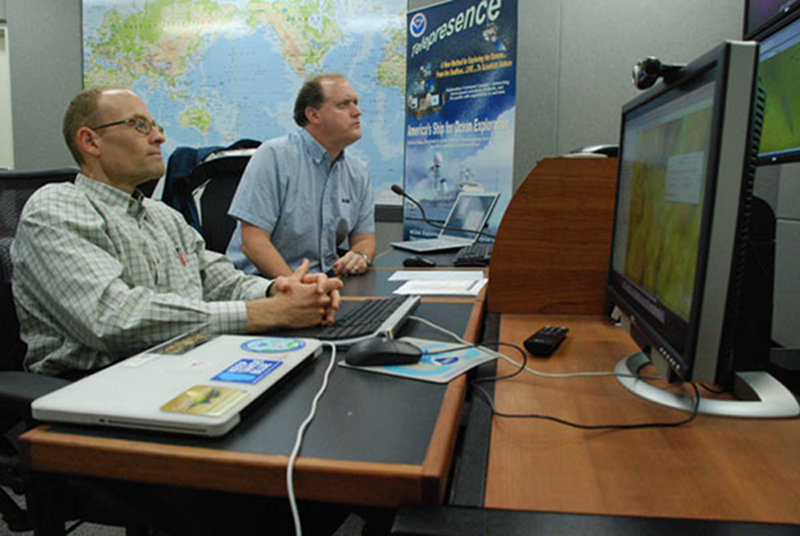 Scientists Scott White (left) and Jim Holden (right) observe the video feed from Little Hercules and record their observations in the Eventlog.