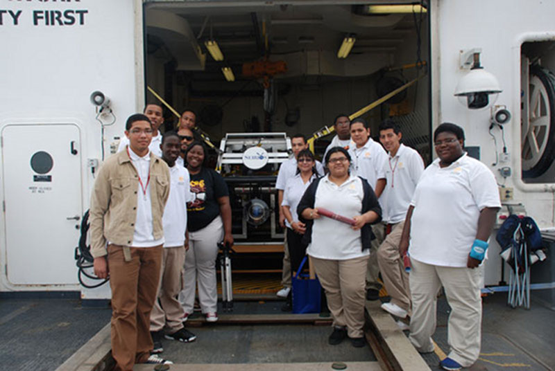 Students from Jack Yates High School Maritime Academy surround the camera sled Seirios in the hangar.