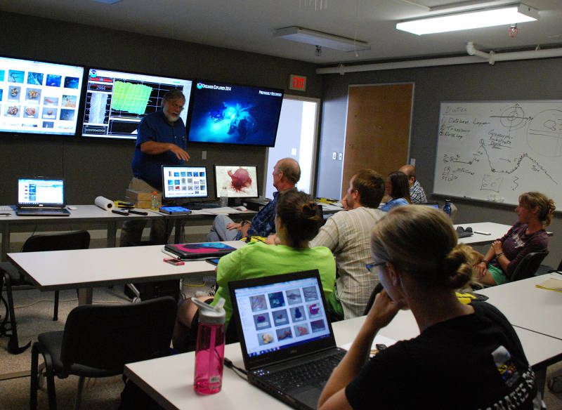 During the 2014 Gulf of Mexico Expedition, only two scientists participated in the cruise onboard NOAA Ship Okeanos Explorer. Via telepresence, the majority of the science team participated from shore - tuning into the live video feeds online and communicating directly with other members of the science team using instant messaging and a teleconference line. Here, Dr. Dennis Hanisak runs through the mission plan with a team of students participating in the expedition from the Harbor Branch Oceanographic Institute Exploration Command Center.