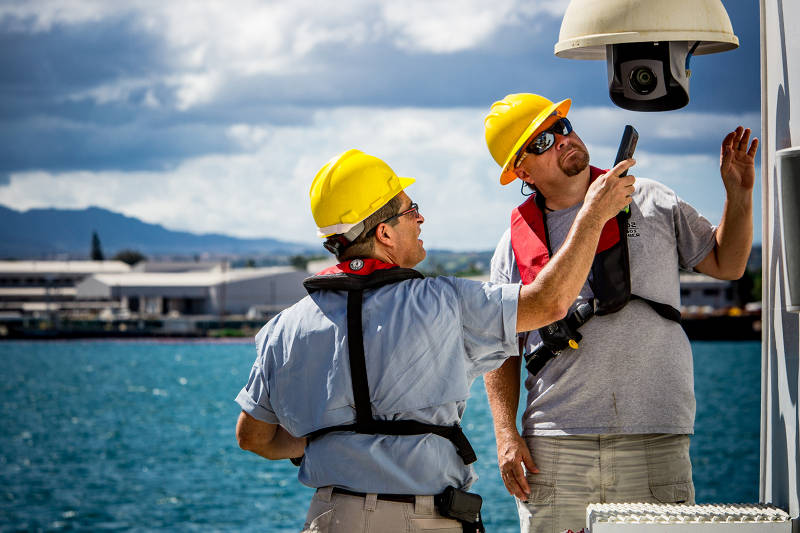 Video engineers Roland Brian and Joe Biscotti work on one of the robotic HD camera’s on the ship’s aft deck while the ship is in port in Pearl Harbor, Oahu.