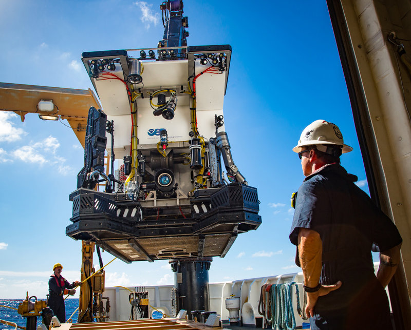 ROV Deep Discoverer (D2) will be used to conduct daily dives from 250 to 6,000 m on Legs 1 and 3 of the 2016 Deepwater Exploration of the Marianas Expedition. Dives will survey seafloor habitats from 250 to 6,000 m, and include high-resolution visual surveys and limited sampling. Here, the Chief Bosun watches as ROV Deep Discoverer (D2) is deployed from the aft deck of NOAA Ship Okeanos Explorer. D2’s powerful lighting, high-definition camera, and sample collection equipment (drawers, boxes, an advanced manipulator, and positionable illumination system) are visible.