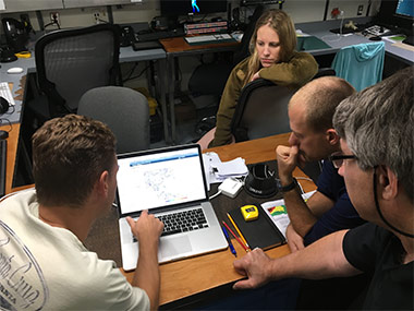 The expedition coordination team and the science lead study the latest forecast.