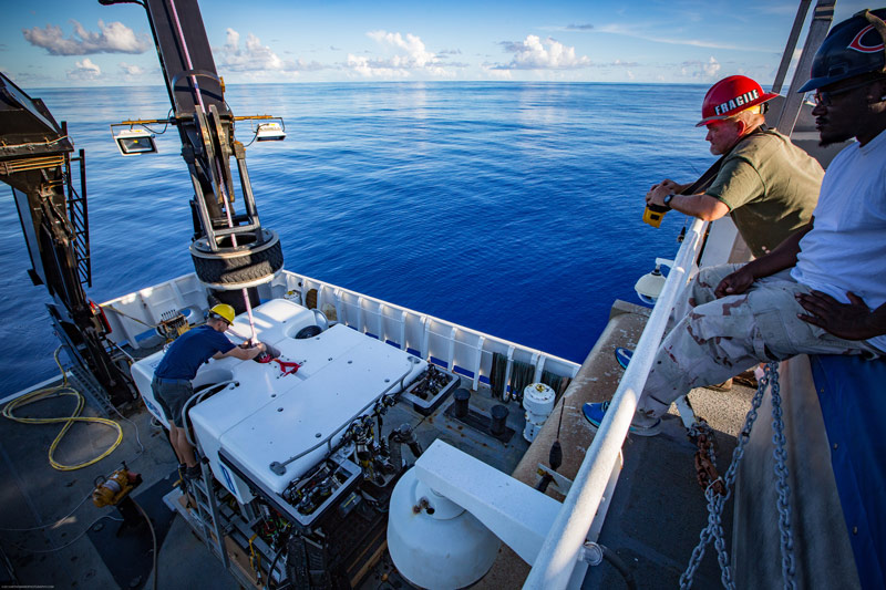 The crew looks on as ROV engineer Chris Ritter attaches the pin securing ROV Deep Discoverer to the lift crane.