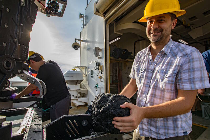 Geology Science Team Lead, Dr. Matthew Jackson, retrieves one of the rocks collected during the dive from the rock box on ROV Deep Discoverer.